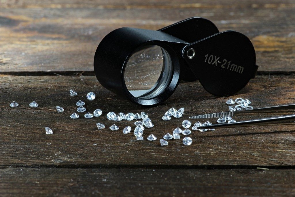 cut diamonds with folding magnifier and tweezers on wooden background