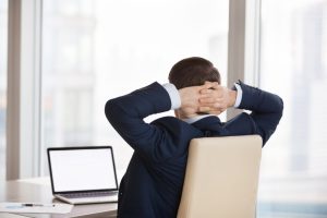 Male employee relaxing at his desk with his hands behind his neck