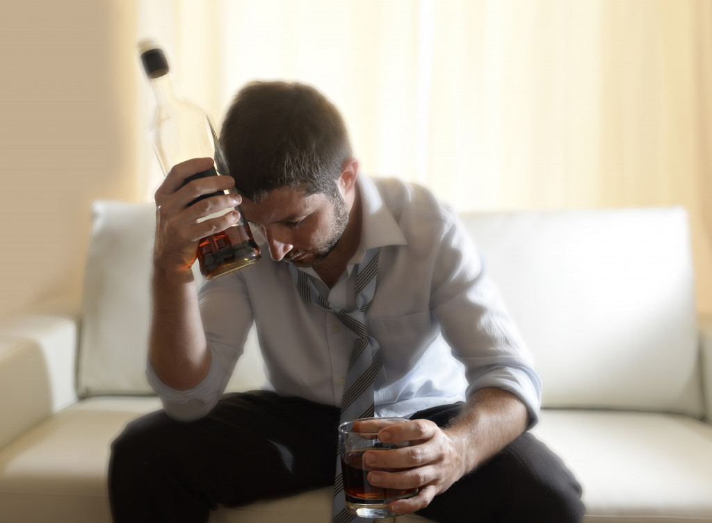 An alcoholic holding a bottle and a drink in a glass