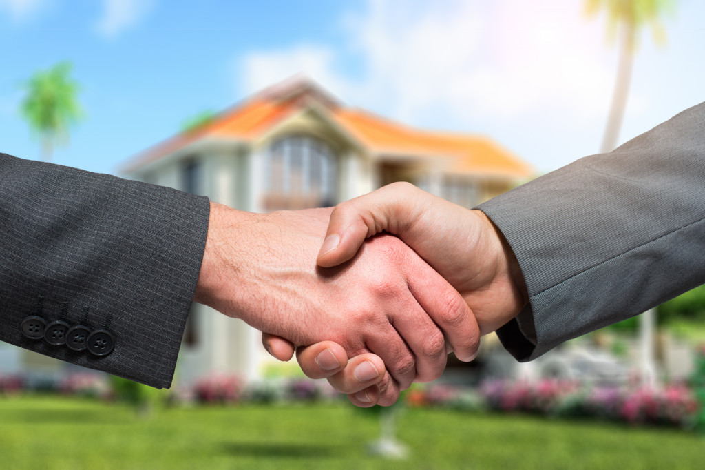 Two business professionals shaking hands in front of a home property